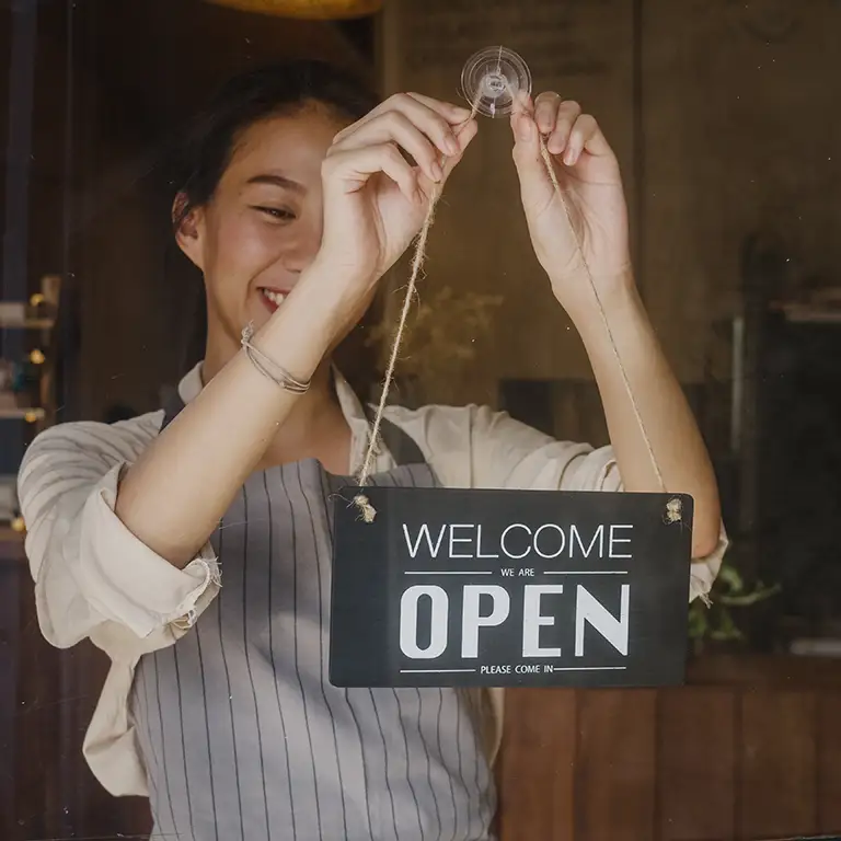 Smiling small to mid-sized business owner hanging an open sign.